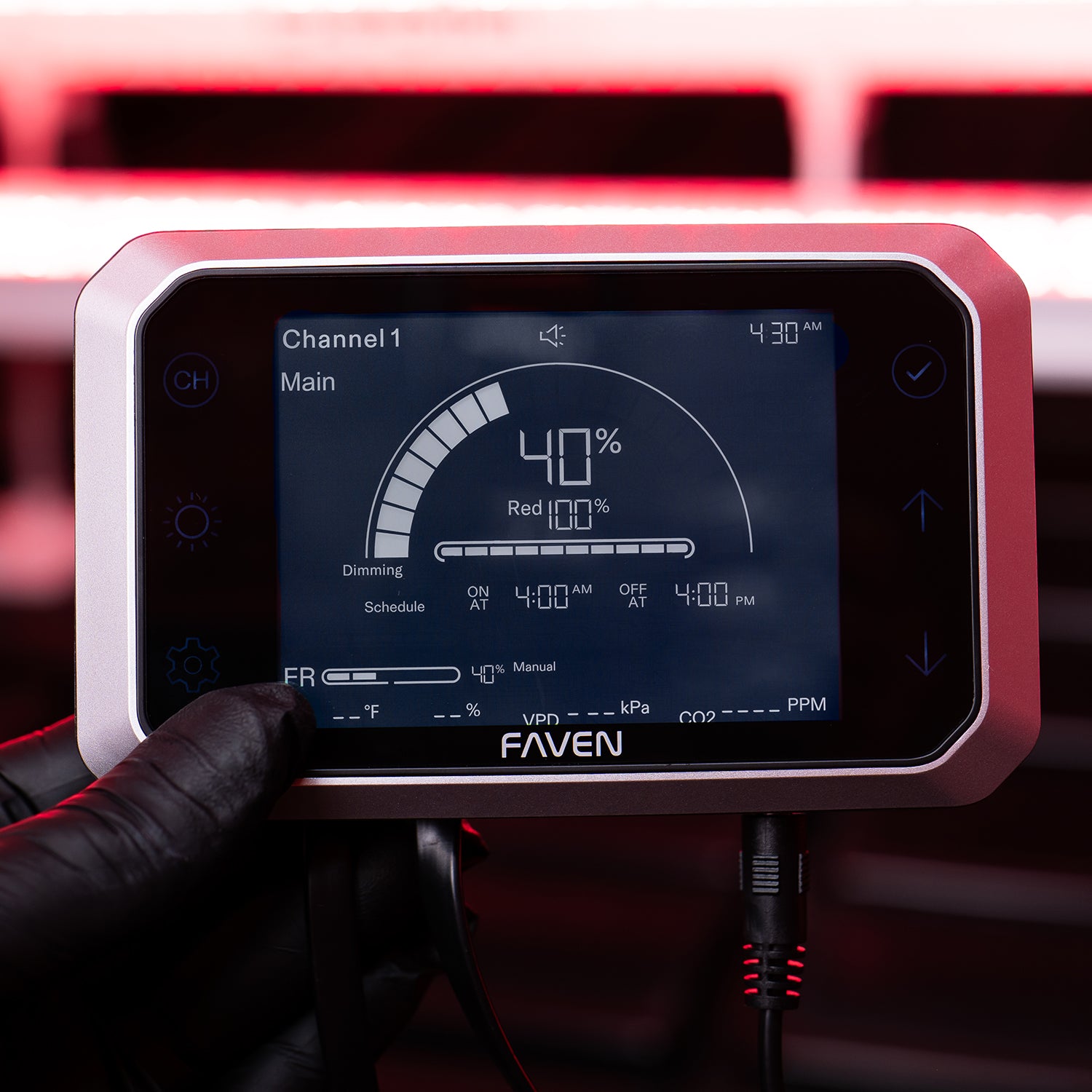 Faven device with the digital display of the Faven Chroma CX2 controllerheld by a gloved hand against a blurred red light background.