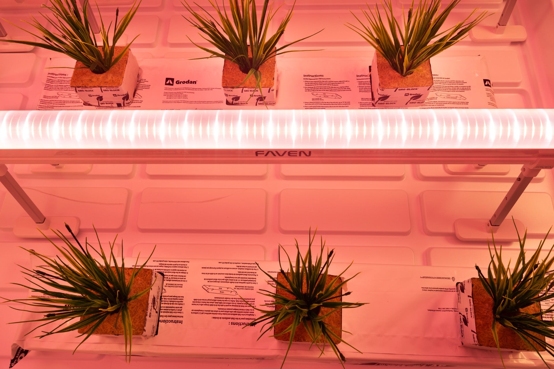 An overhead view of a Faven LED under canopy set to a far red spctrum next to fake house plants on a white background. 
